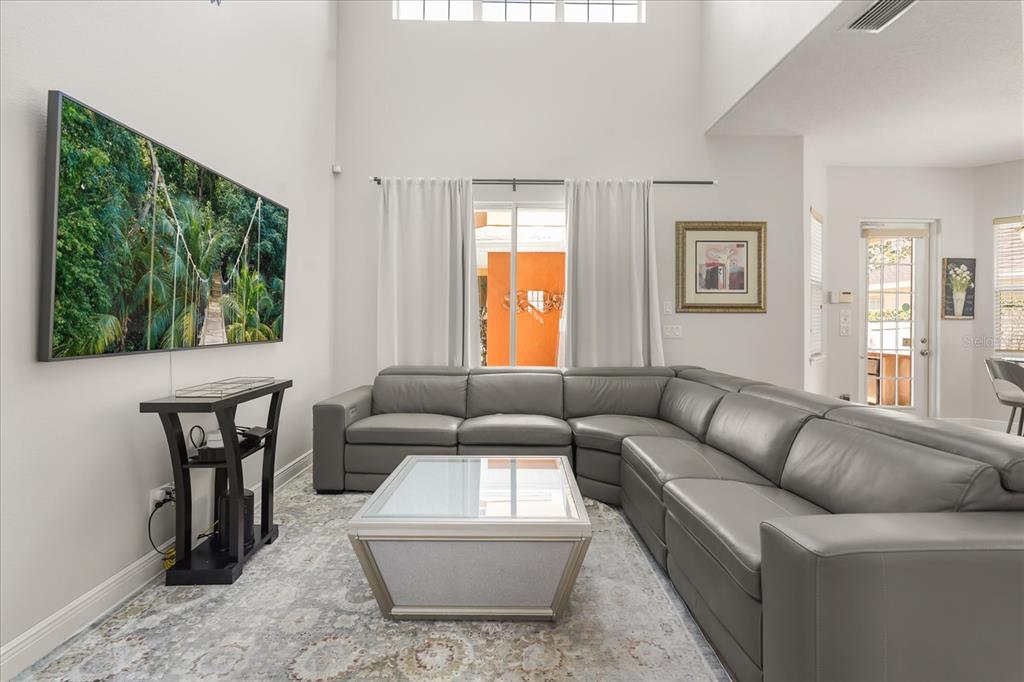 A living room with a gray sectional sofa, a glass coffee table, and a wall-mounted television — 7708 EXCITEMENT DRIVE, REUNION, FL