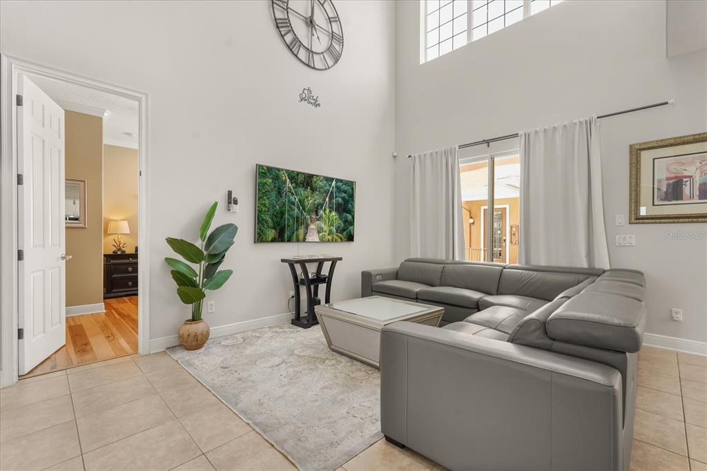 A living room features a gray sectional sofa, a wall-mounted television, and high ceilings — 7708 EXCITEMENT DRIVE, REUNION, FL