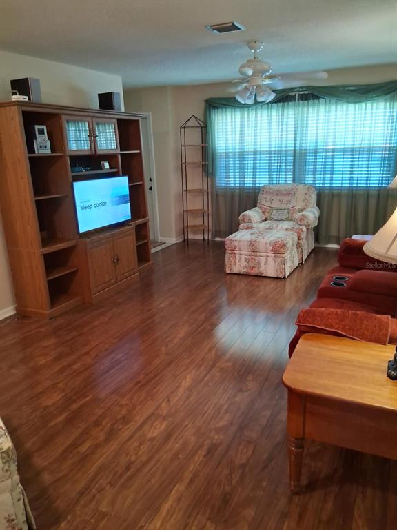 A living room features wood flooring, a large entertainment center, and a floral armchair — 6770 RIVIERA N, PINELLAS PARK, FL