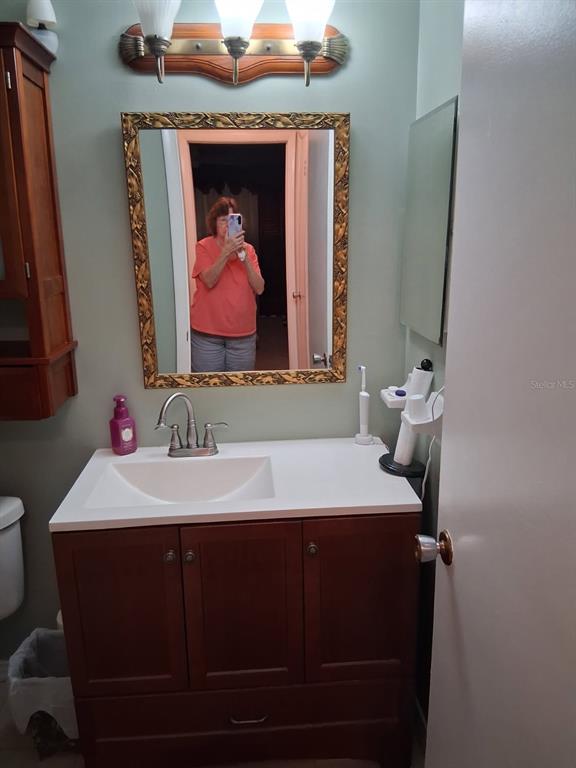 A bathroom vanity with a white countertop, wooden cabinet, and a framed mirror on the wall — 6770 RIVIERA N, PINELLAS PARK, FL