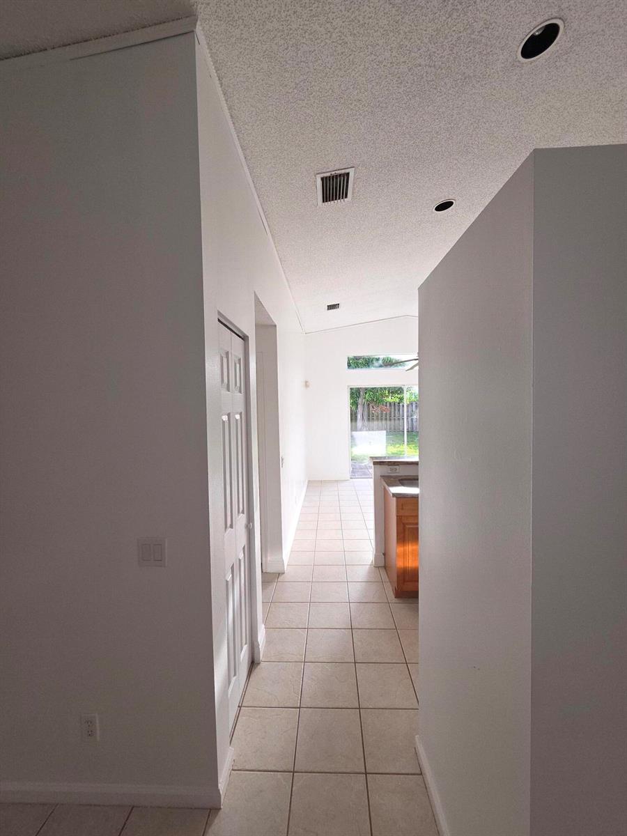A hallway with tiled floors leads toward a kitchen and a sliding glass door — 7093 Middlebury Drive # 7093, Boynton Beach FL 33436, BOYNTON BEACH, FL