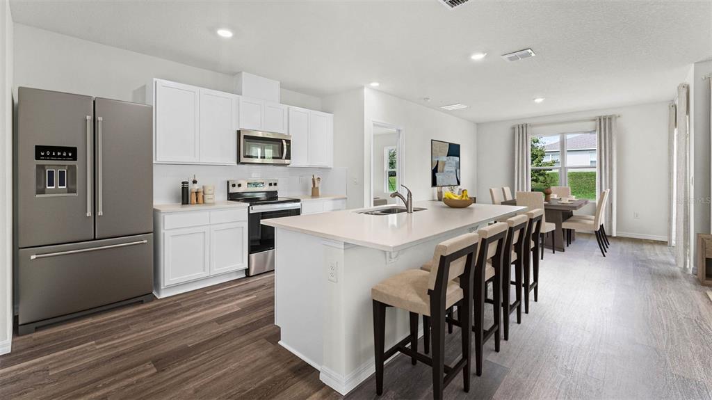 A modern kitchen features white cabinets, stainless steel appliances, a center island, and wood flooring — 5175 NICKERBEAN STREET, APOPKA, FL