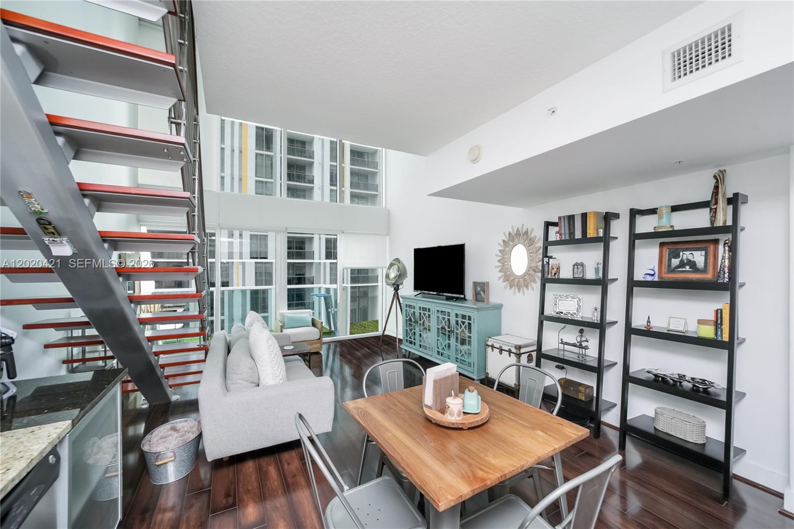 A modern living and dining area features a floating staircase, floor-to-ceiling windows, and hardwood floors — 41 SE 5th St # 704, Miami FL 33131, MIAMI, FL