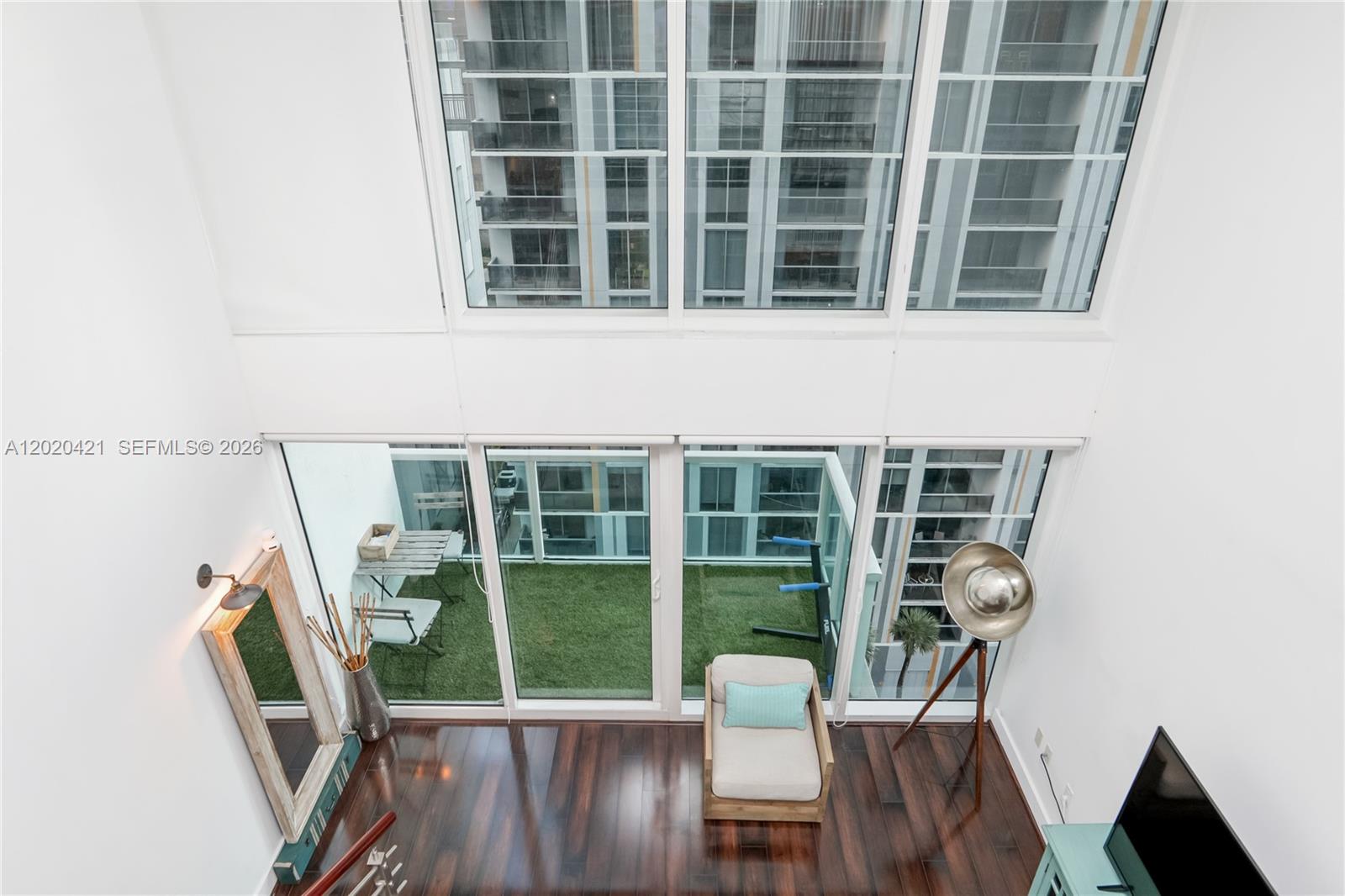 A high-ceiling living room features dark wood floors, a balcony with artificial turf, and floor-to-ceiling windows — 41 SE 5th St # 704, Miami FL 33131, MIAMI, FL