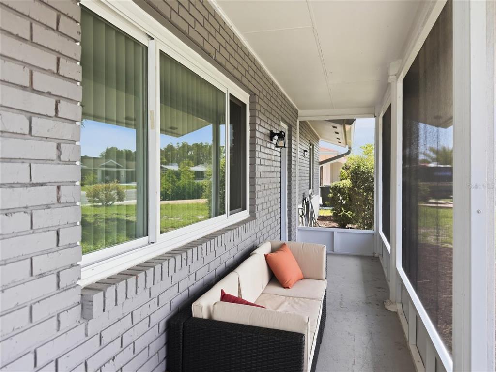 A covered porch features gray brick walls, a screened enclosure, and a wicker sofa — 1404 SETON HALL DRIVE, SUN CITY CENTER, FL