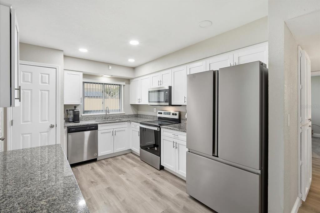 A kitchen features white cabinets, stainless steel appliances, granite countertops, and light wood-look flooring — 1404 SETON HALL DRIVE, SUN CITY CENTER, FL