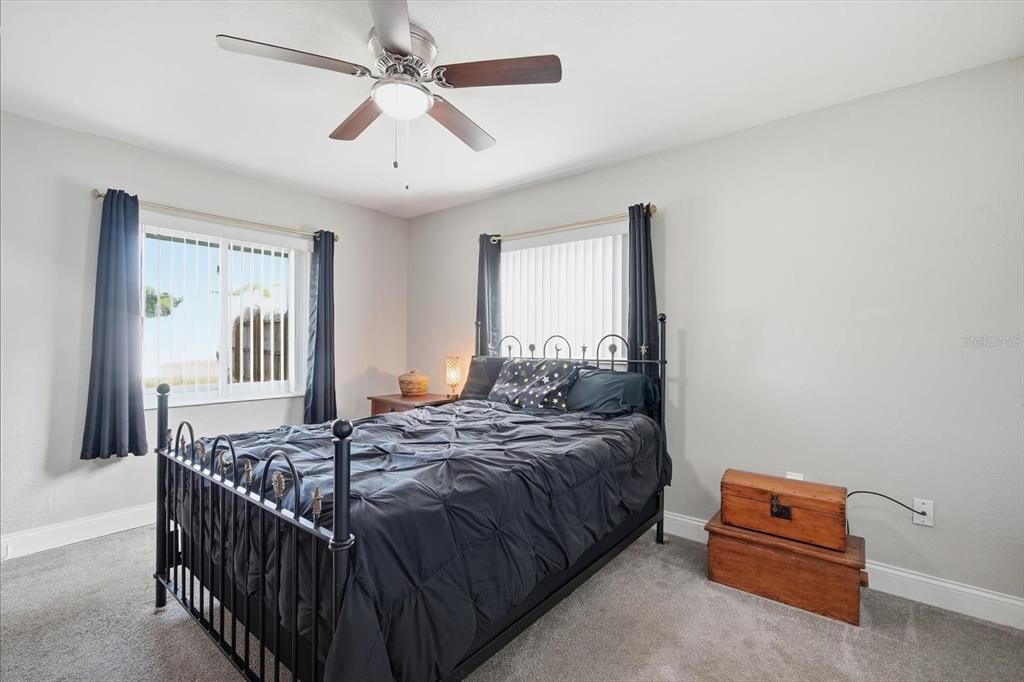A bedroom features a black metal bed frame, gray carpet, and two windows with curtains — 1404 SETON HALL DRIVE, SUN CITY CENTER, FL