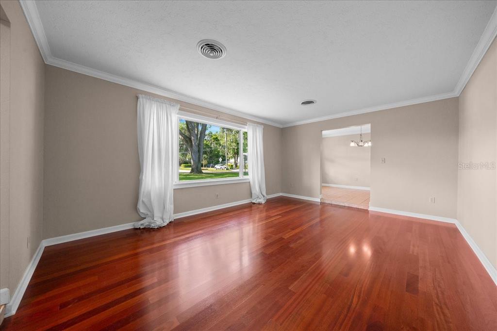 An empty living room features hardwood floors, white walls, and a large window with curtains — 2009 SE 15TH LANE, OCALA, FL