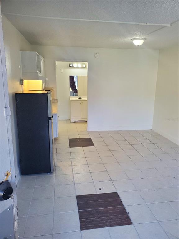 A small kitchen area with a black refrigerator, white cabinets, and light-colored floor tiles — 7900 S ORANGE BLOSSOM TRAIL UNIT 1120, ORLANDO, FL