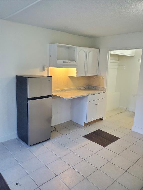 A small kitchen features white cabinets, a stainless steel refrigerator, and light-colored tile flooring — 7900 S ORANGE BLOSSOM TRAIL UNIT 1120, ORLANDO, FL