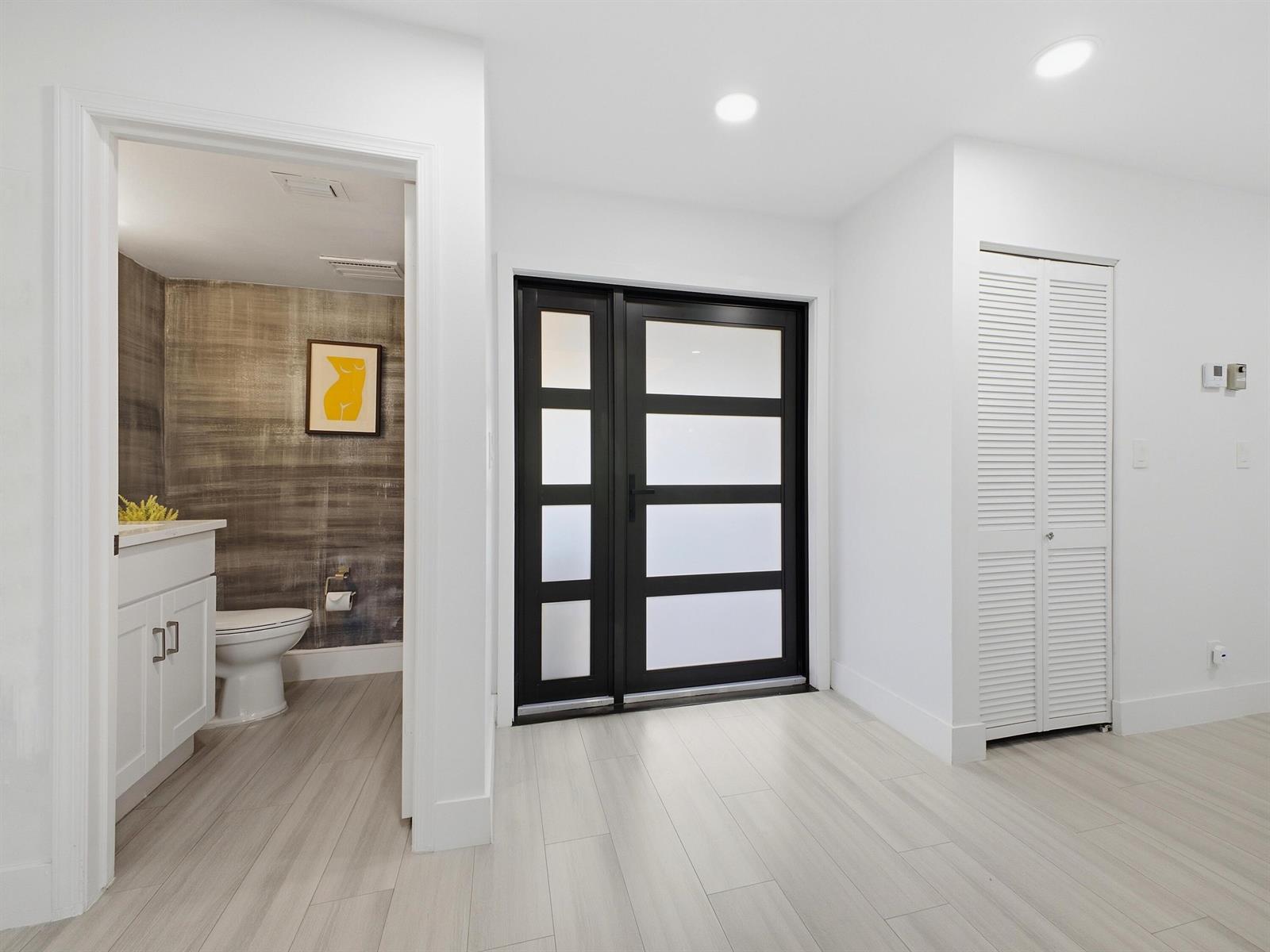 A modern entryway features light wood-look flooring, a black-framed glass door, and an adjacent bathroom — 20539 Linksview Way, Boca Raton FL 33434, BOCA RATON, FL