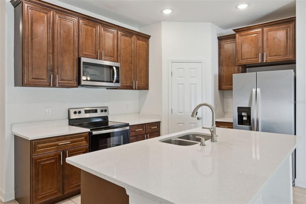 A kitchen features wood cabinets, stainless steel appliances, and a white quartz island countertop — 2505 BAKER AVENUE E, HAINES CITY, FL