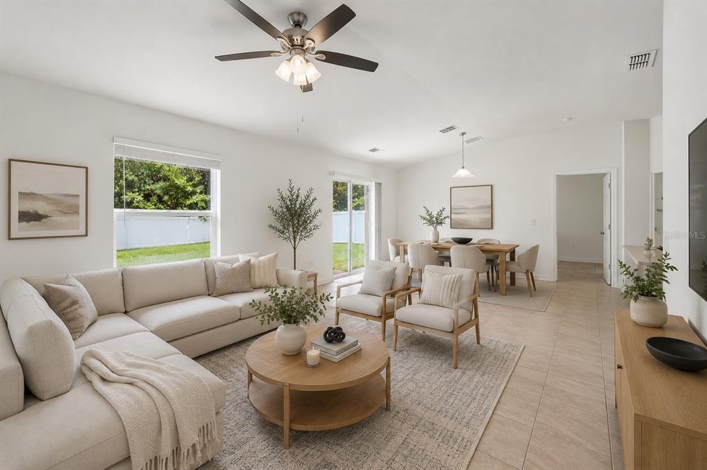 A bright, open-concept living and dining area features neutral furniture, tile flooring, and sliding doors — 2505 BAKER AVENUE E, HAINES CITY, FL
