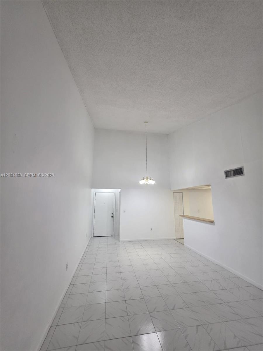 A high-ceilinged room features white walls, light-colored tiled flooring, and a hanging light fixture — 9429 Fontainebleau Blvd # 33, Miami FL 33172, MIAMI, FL