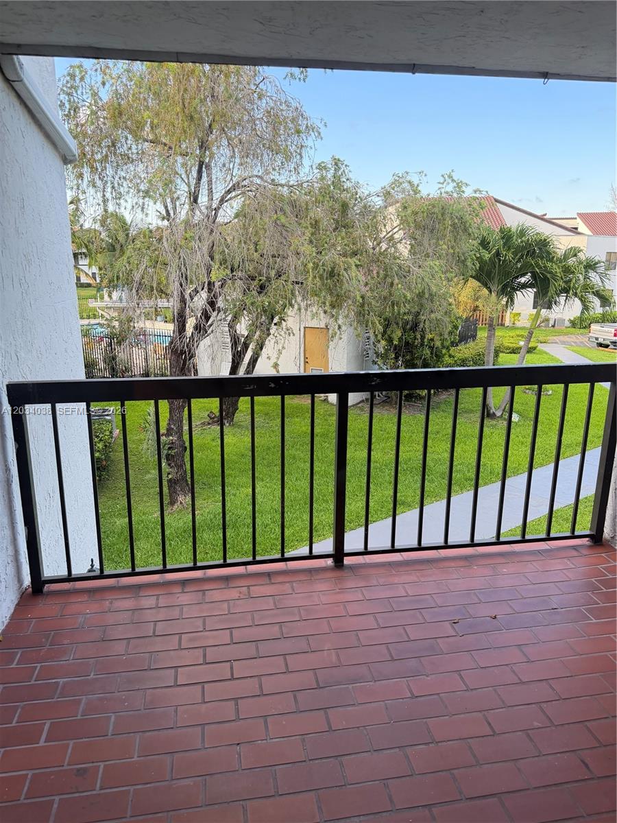 A balcony with red brick flooring and a black metal railing overlooks a grassy courtyard — 9429 Fontainebleau Blvd # 33, Miami FL 33172, MIAMI, FL