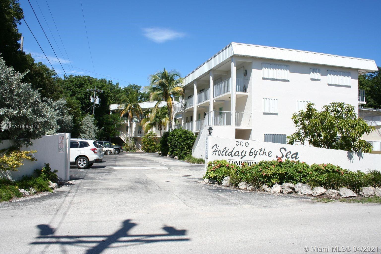 The exterior of a white multi-story condominium building features a parking area and palm trees — 300 Ocean Drive # 20, Key Largo FL 33037, KEY LARGO, FL
