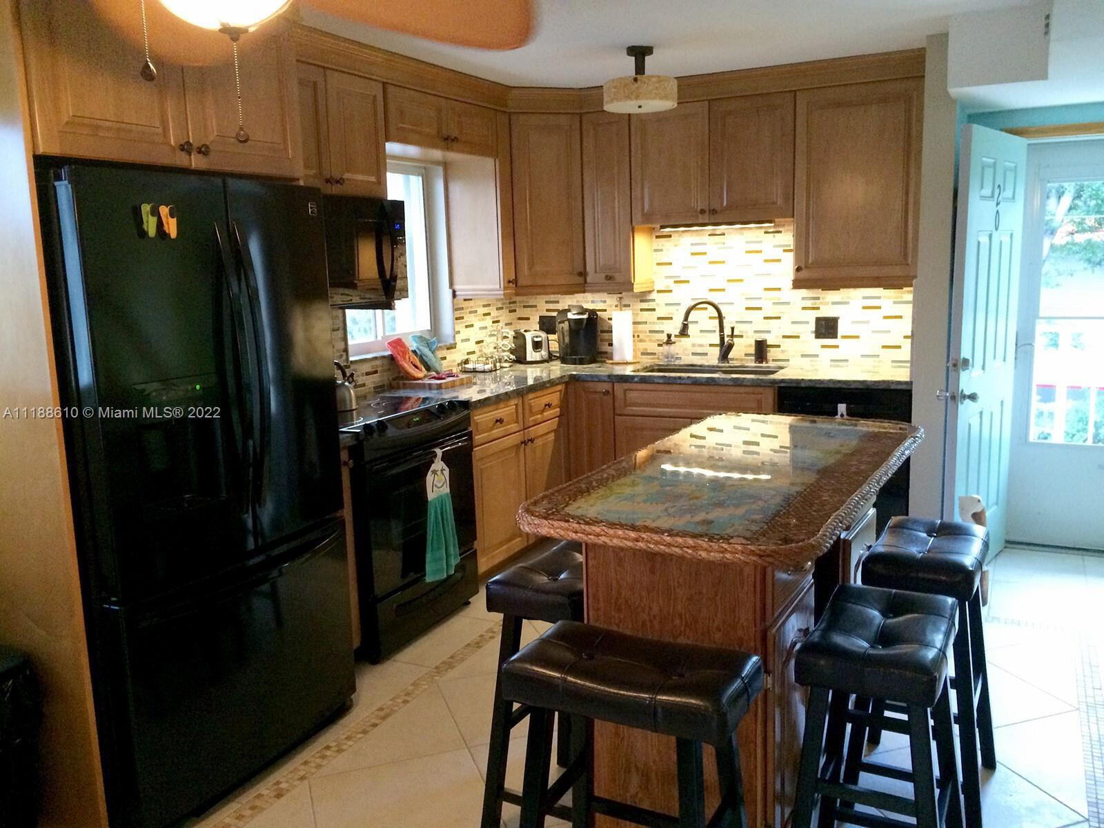 A kitchen features wood cabinets, black appliances, a tiled backsplash, and a central island — 300 Ocean Drive # 20, Key Largo FL 33037, KEY LARGO, FL