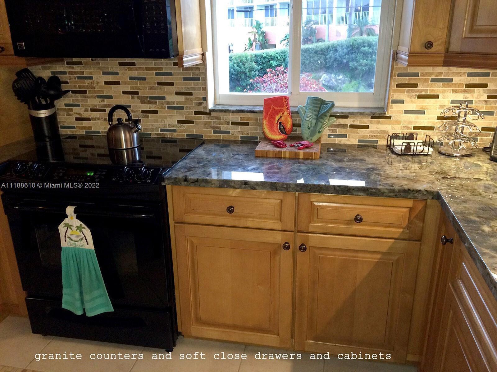 A kitchen features wood cabinets, granite countertops, a black stove, and a tiled backsplash — 300 Ocean Drive # 20, Key Largo FL 33037, KEY LARGO, FL