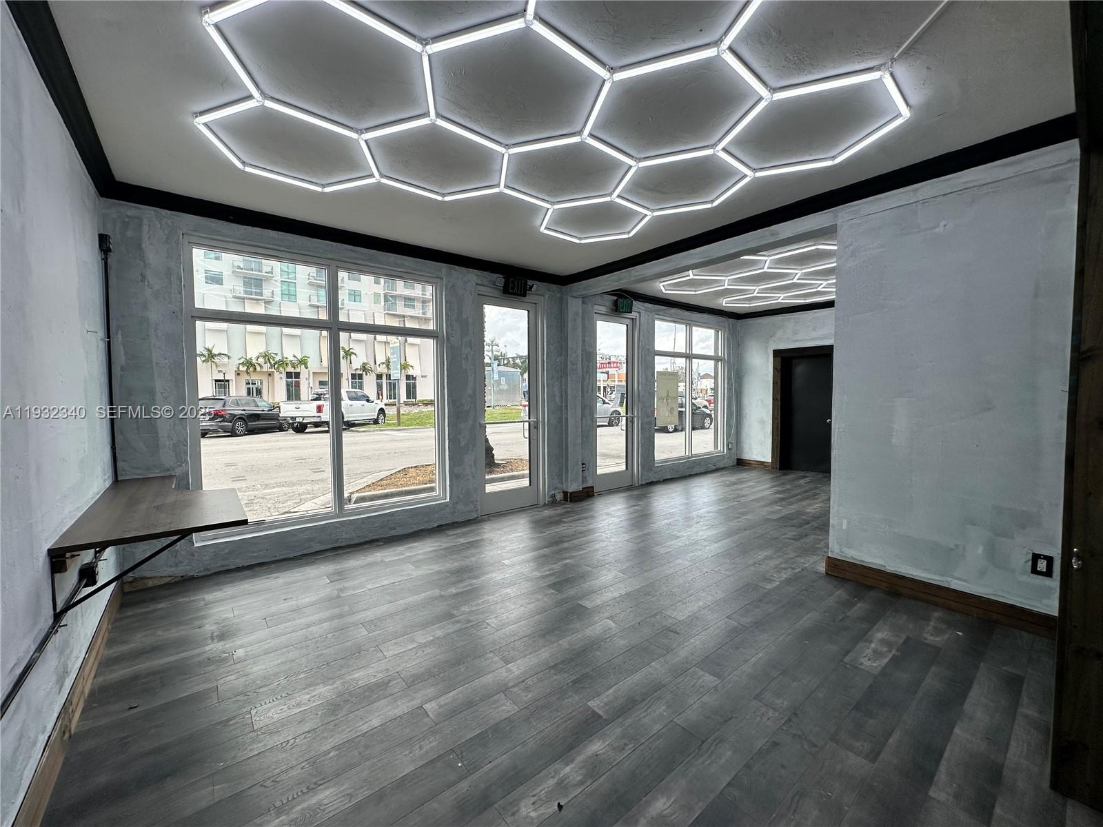 An empty commercial space features gray wood-look flooring, textured walls, and hexagonal ceiling lighting — 111 S 21 Ave, Hollywood FL 33020, HOLLYWOOD, FL