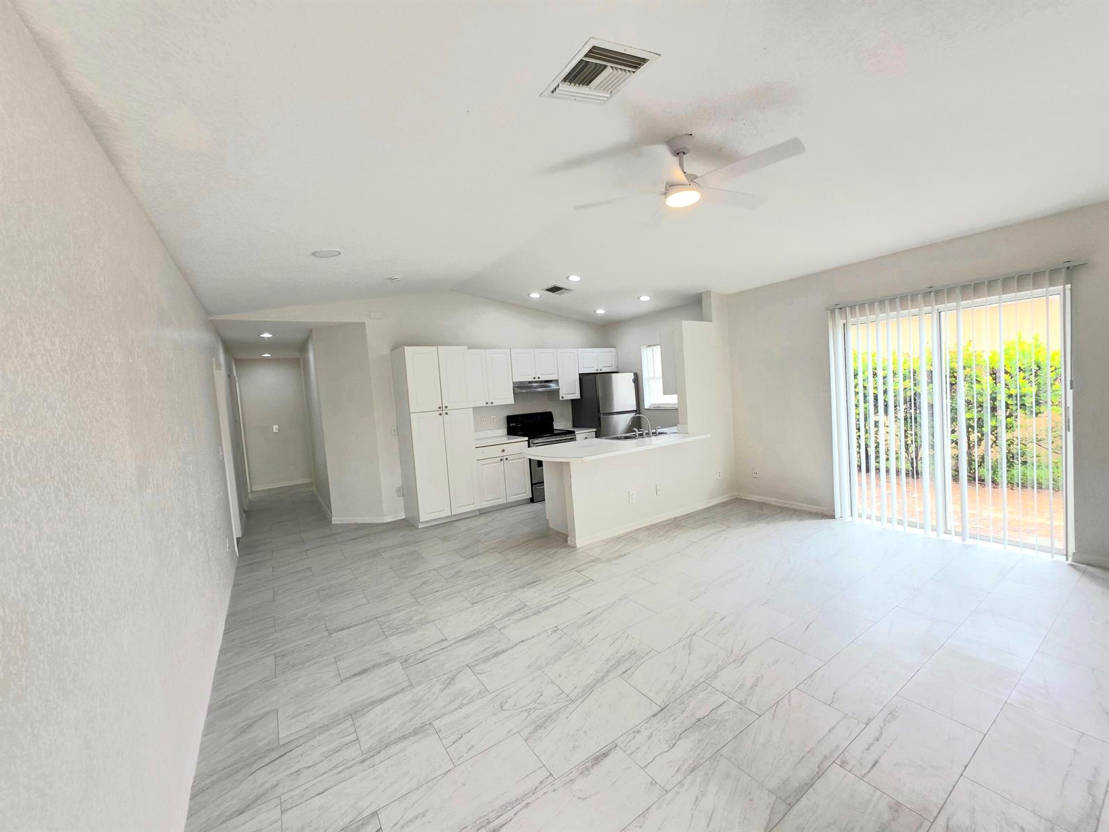 An open-concept kitchen and living area features white cabinetry, stainless appliances, and light tile flooring — 569 E Ridge Circle N, Boynton Beach FL 33435, BOYNTON BEACH, FL