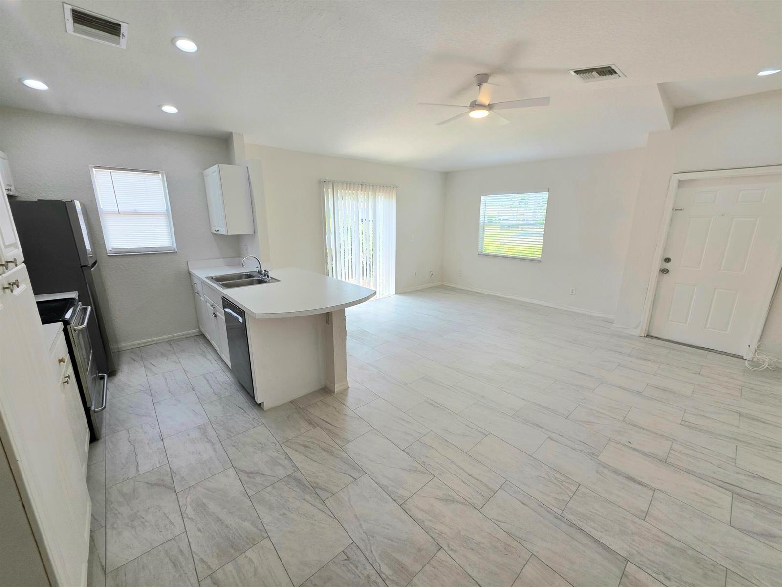 An open-concept kitchen and living area featuring white cabinetry, stainless appliances, and light tile flooring — 569 E Ridge Circle N, Boynton Beach FL 33435, BOYNTON BEACH, FL