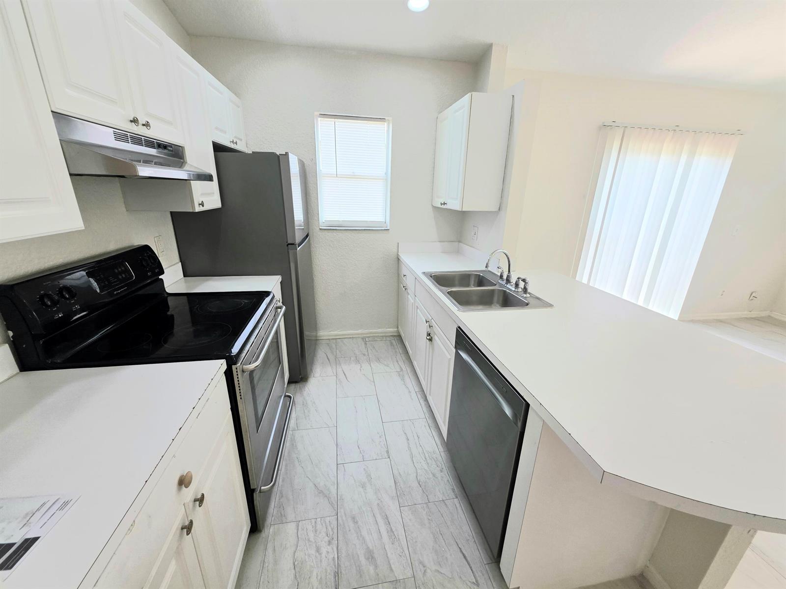 A kitchen features white cabinets, dark appliances, a double sink, and light-colored tile flooring — 569 E Ridge Circle N, Boynton Beach FL 33435, BOYNTON BEACH, FL