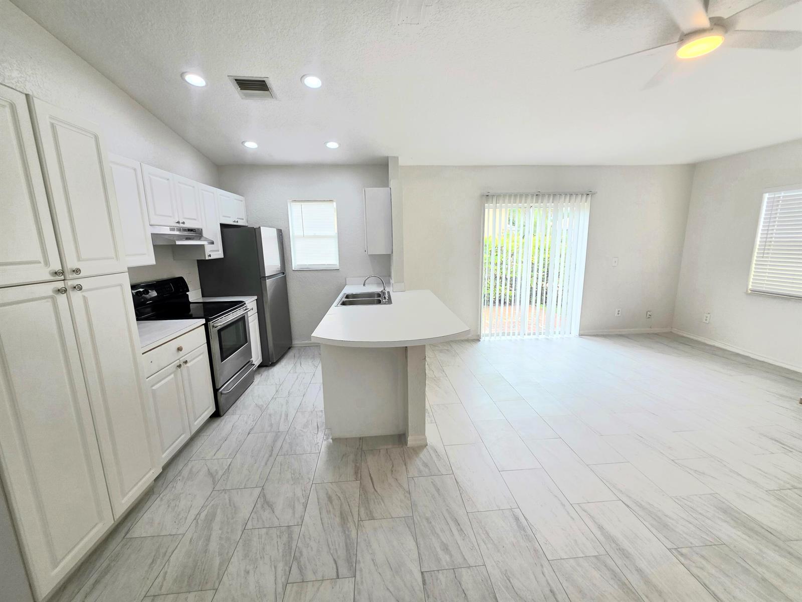 A kitchen with white cabinets, stainless steel appliances, and light tile flooring opens to a living area — 569 E Ridge Circle N, Boynton Beach FL 33435, BOYNTON BEACH, FL