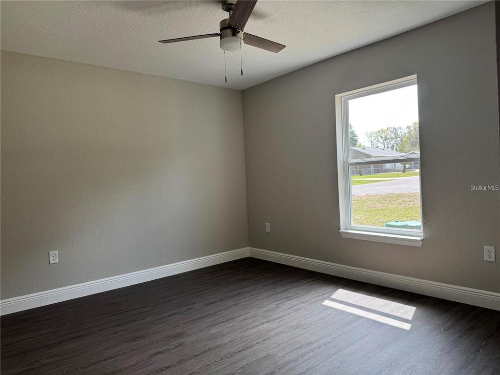 An empty bedroom features gray walls, dark wood-look flooring, a ceiling fan, and a window — 3957 SE 137TH LANE, SUMMERFIELD, FL