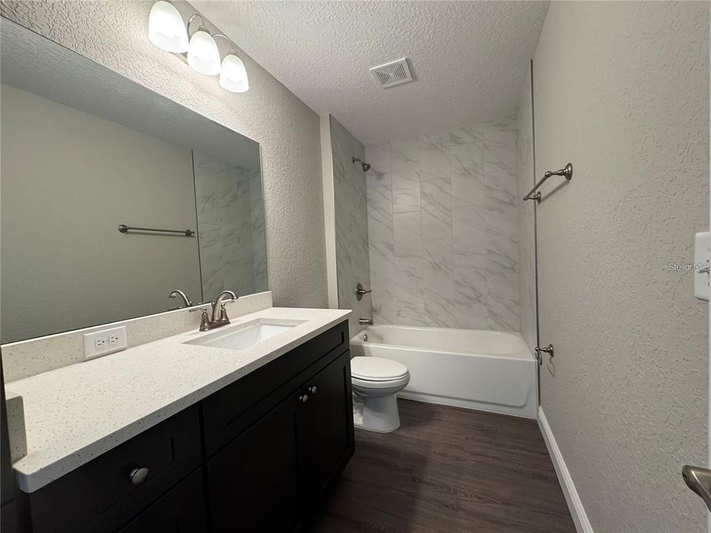 A bathroom features a dark vanity, a white countertop, and a tub with marble-look tile — 3957 SE 137TH LANE, SUMMERFIELD, FL