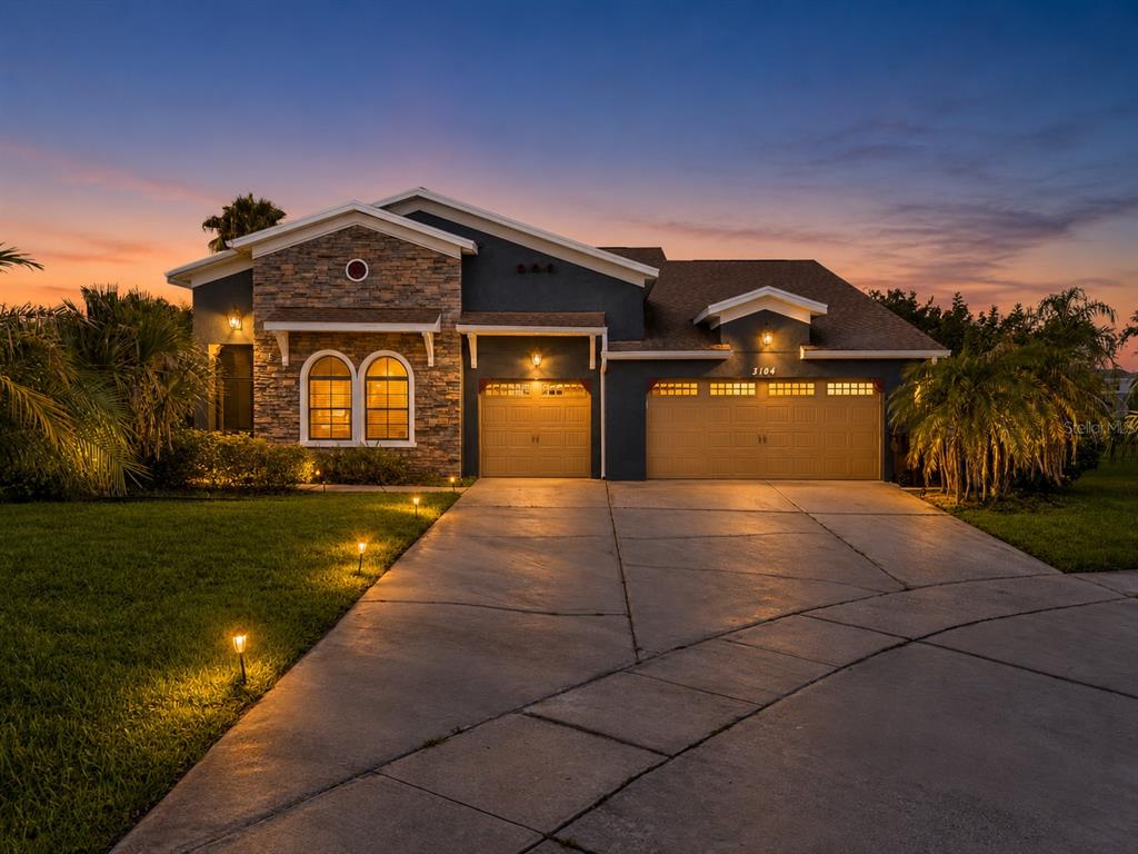 A single-story house with a stone facade, dark blue siding, and a three-car garage at dusk — 3104 BASS BOAT WAY, KISSIMMEE, FL