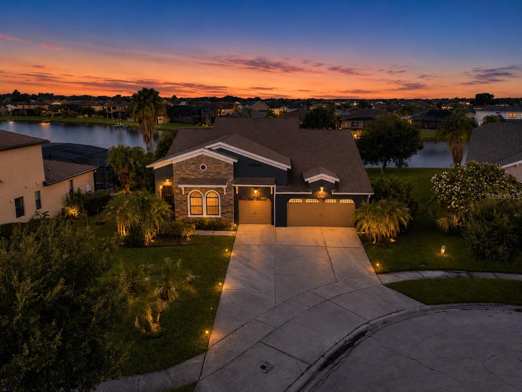 An aerial view of a single-story house with a stone facade, three-car garage, and lakefront backyard — 3104 BASS BOAT WAY, KISSIMMEE, FL