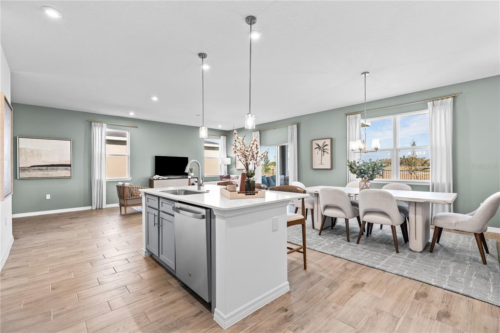 An open-concept kitchen and dining area featuring a central island, light wood flooring, and furniture — 10108 MORNING MEADOWLARK TRAIL, PARRISH, FL