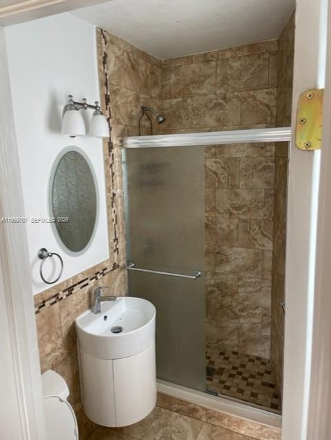 A small bathroom features a pedestal sink, a round mirror, and a tiled walk-in shower — 2121 Biarritz Dr # 5, Miami Beach FL 33141, MIAMI BEACH, FL