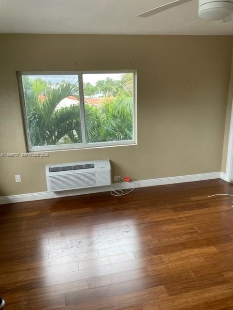 A room with wood flooring, a window overlooking palm trees, and a wall-mounted air conditioner — 2121 Biarritz Dr # 5, Miami Beach FL 33141, MIAMI BEACH, FL