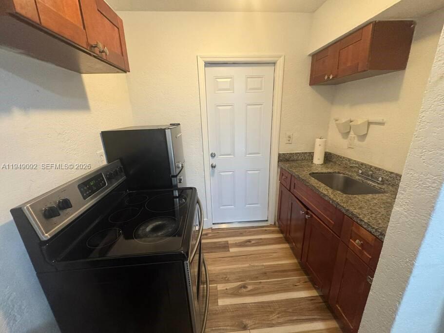 A small kitchen features dark wood cabinets, granite countertops, a black stove, and wood-look flooring — 7638 N Miami Avenue # 4, Miami FL 33150, MIAMI, FL