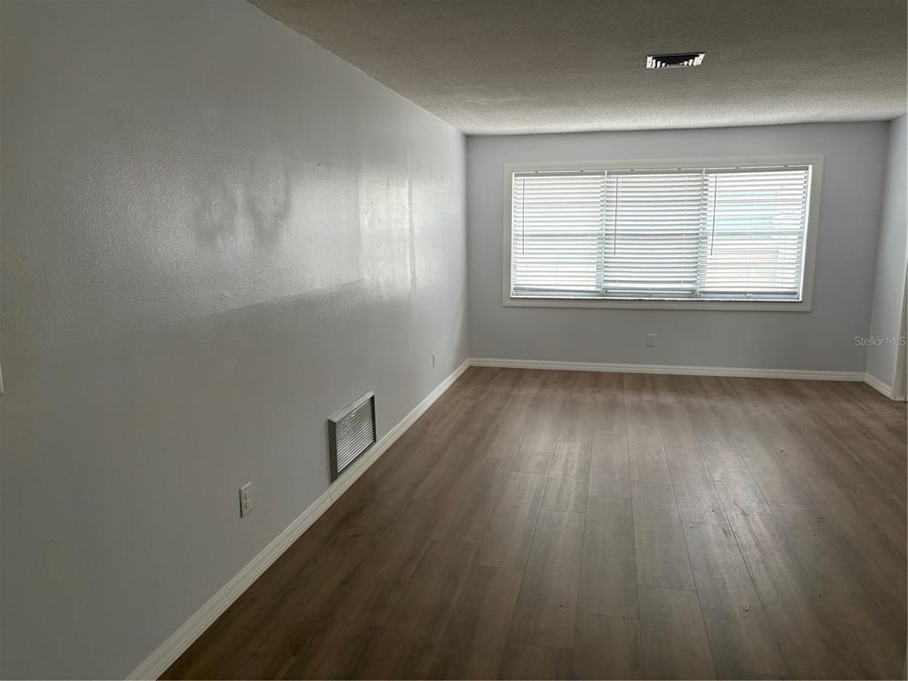 An empty room features light gray walls, wood-look flooring, and a large window with blinds — 2380 TIMBERCREST CIRCLE W, CLEARWATER, FL