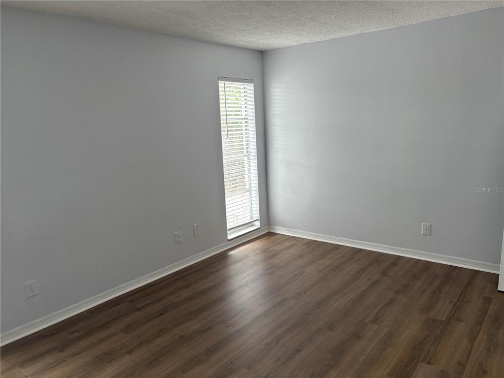 An empty room features light gray walls, wood-look flooring, and a single window with blinds — 2380 TIMBERCREST CIRCLE W, CLEARWATER, FL