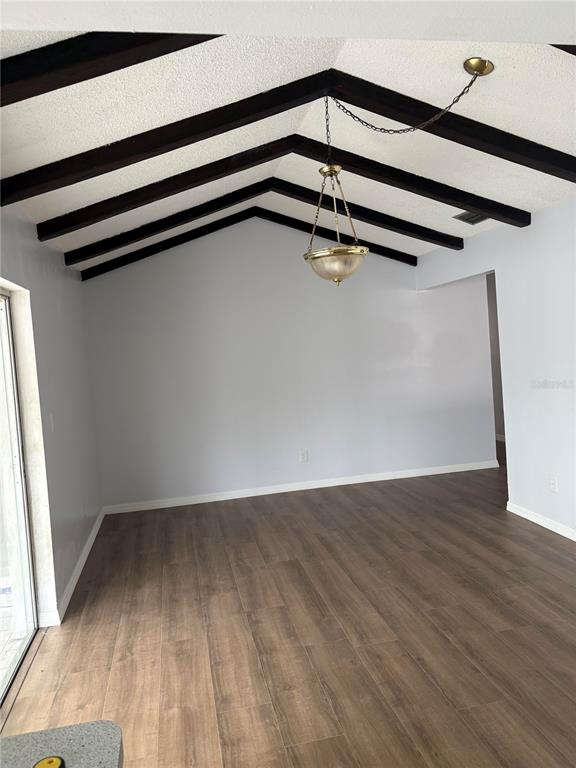 An empty room features wood-look flooring, light gray walls, and a vaulted ceiling with exposed beams — 2380 TIMBERCREST CIRCLE W, CLEARWATER, FL