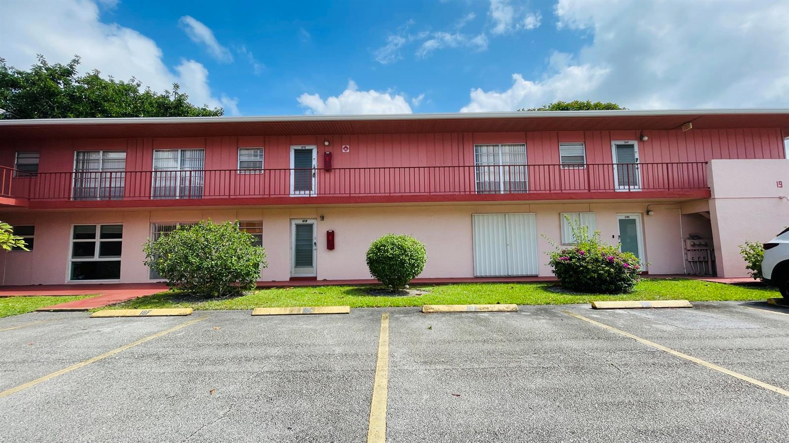 A two-story pink apartment building with a red balcony and a parking lot in front — 19 Golfs Edge, West Palm Beach FL 33417, WEST PALM BEACH, FL