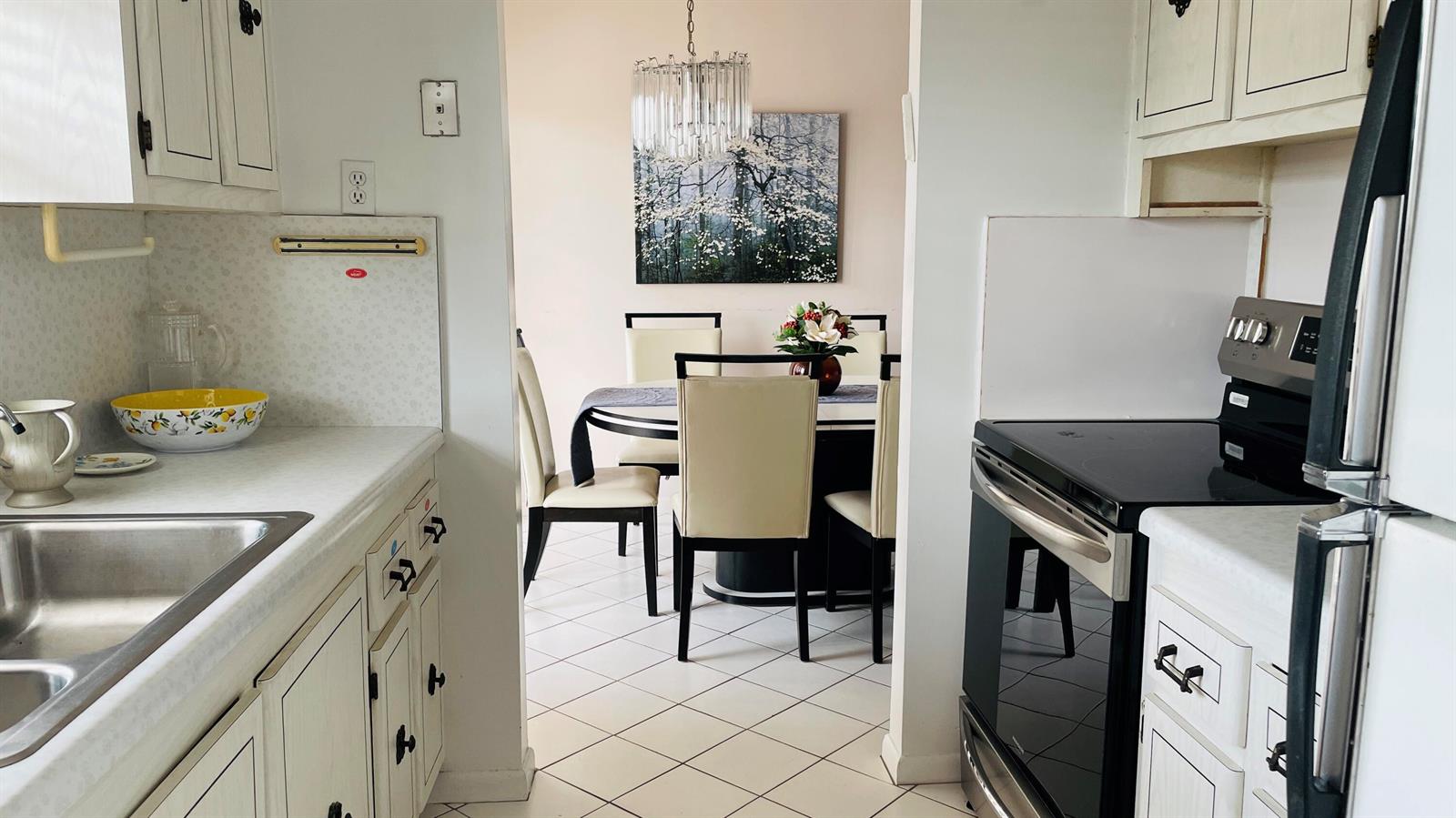 A kitchen with white cabinets and a stainless steel stove opens into a dining area — 19 Golfs Edge, West Palm Beach FL 33417, WEST PALM BEACH, FL