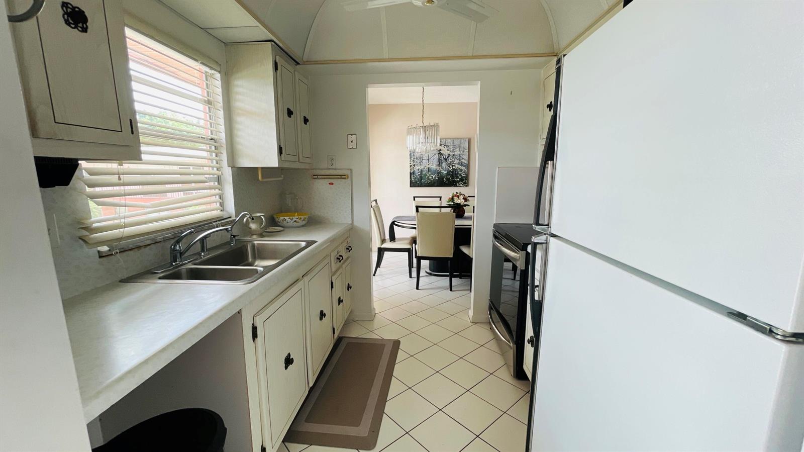 A kitchen with white cabinets, a double sink, and tile flooring leads to a dining area — 19 Golfs Edge, West Palm Beach FL 33417, WEST PALM BEACH, FL
