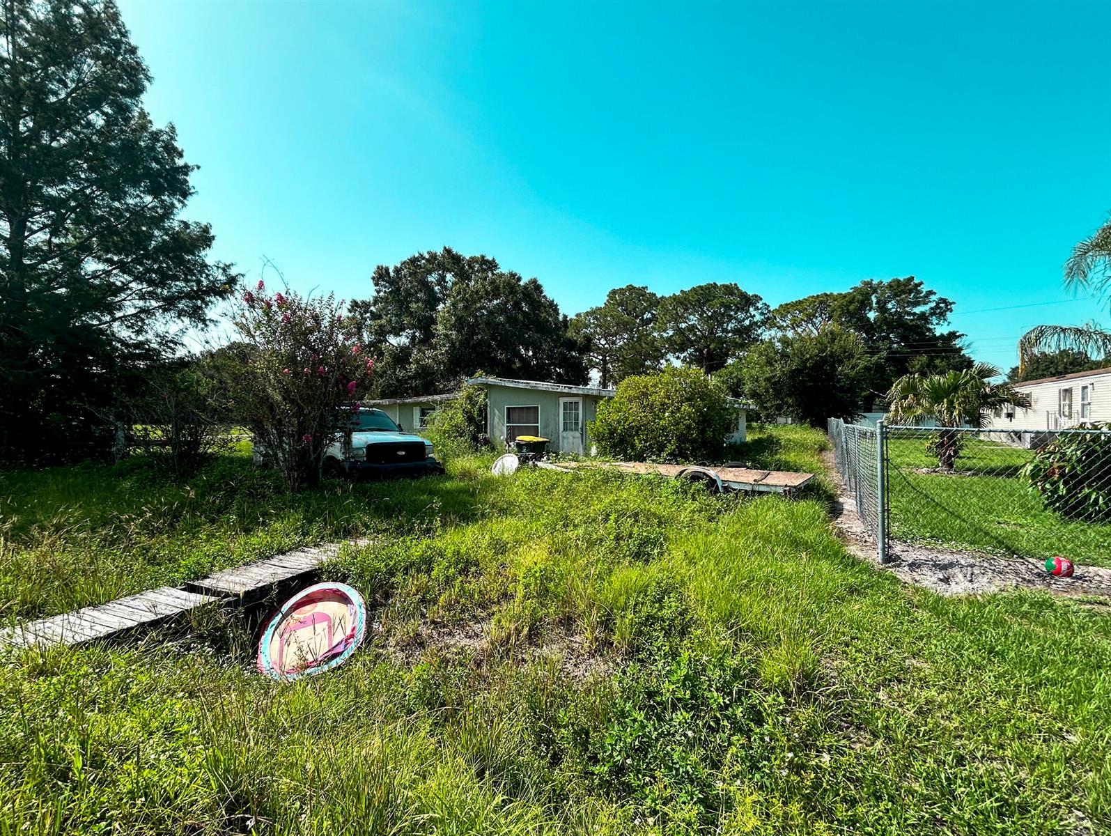 A grassy yard with a parked truck, a trailer, and a small house in the background — 17202 Broadland Lane, Okeechobee FL 34974, OKEECHOBEE, FL