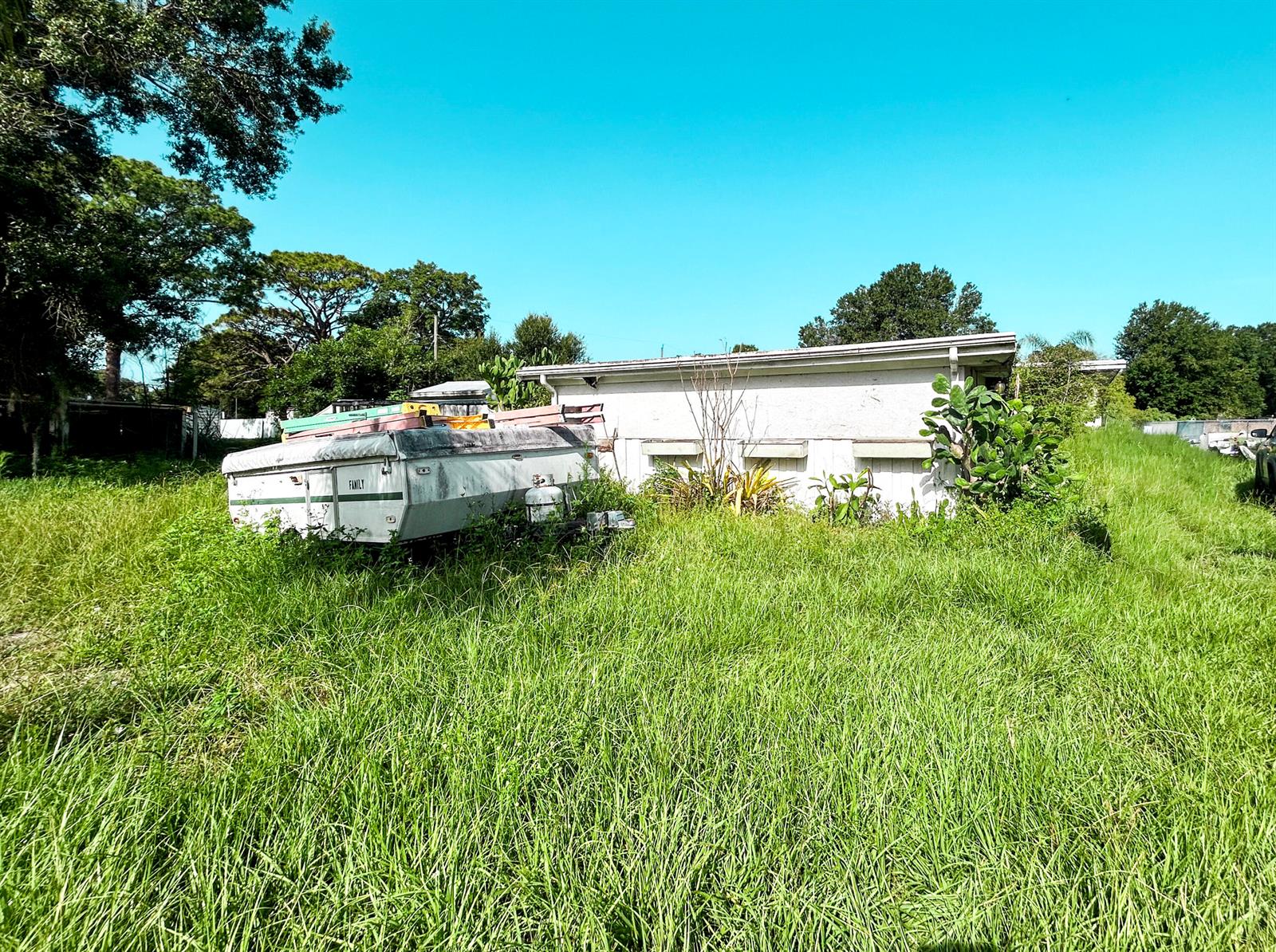 A pop-up camper sits in a tall, grassy yard next to a white building — 17202 Broadland Lane, Okeechobee FL 34974, OKEECHOBEE, FL