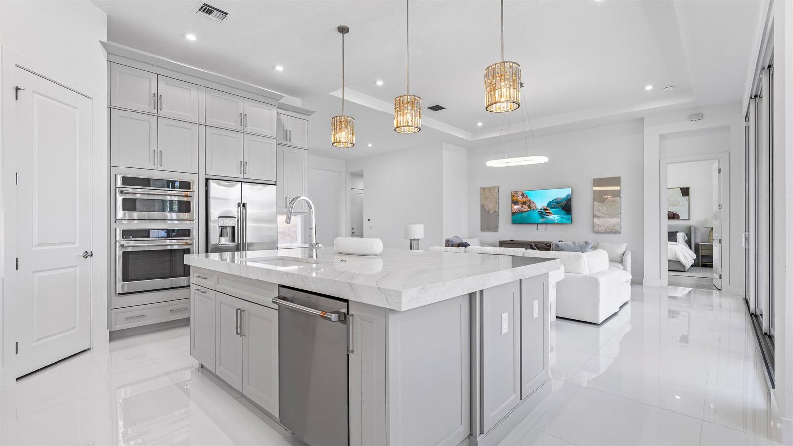 A modern kitchen features a large marble-topped island, gray cabinetry, and stainless steel appliances — 9508 St. Germain, Palm Beach Gardens FL 33412, PALM BEACH GARDENS, FL