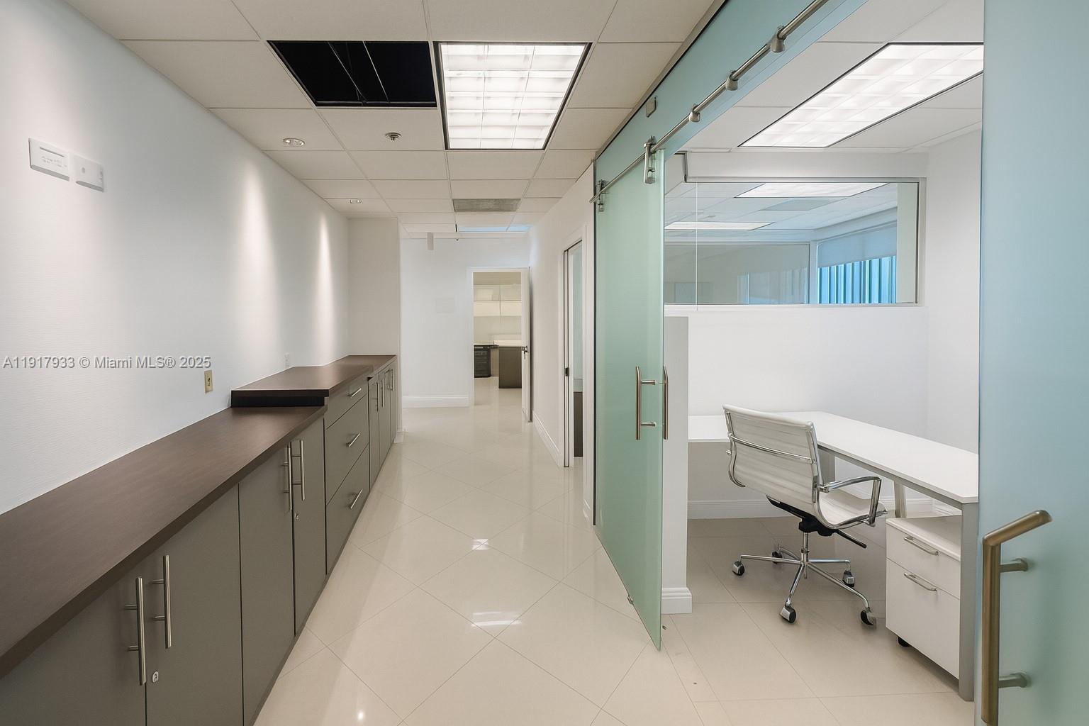 A modern office hallway features gray cabinetry, a glass sliding door, and a white desk — 1000 5th St # 304, Miami Beach FL 33139, MIAMI BEACH, FL
