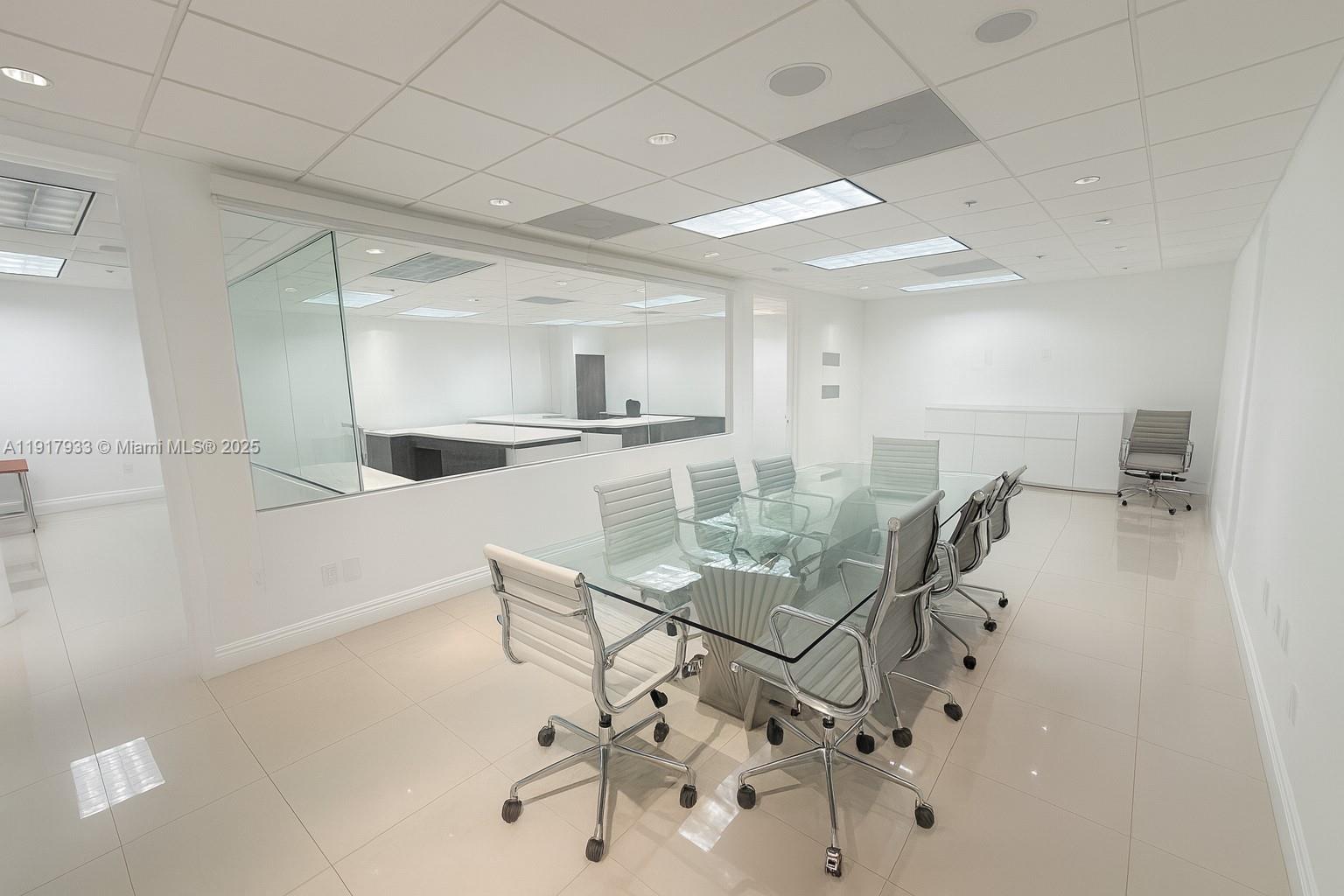 A modern conference room features a glass-topped table, white chairs, and a large interior window — 1000 5th St # 304, Miami Beach FL 33139, MIAMI BEACH, FL