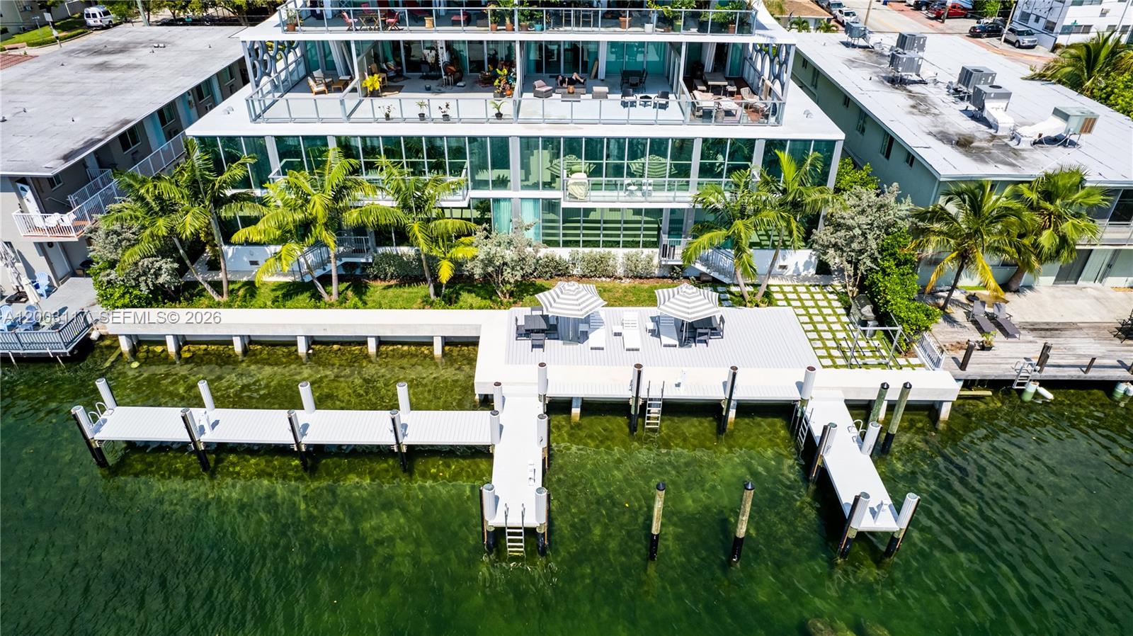 An aerial view shows a modern waterfront building with a deck, dock, and palm trees — 8425 Crespi Blvd, Miami Beach FL 33141, MIAMI BEACH, FL