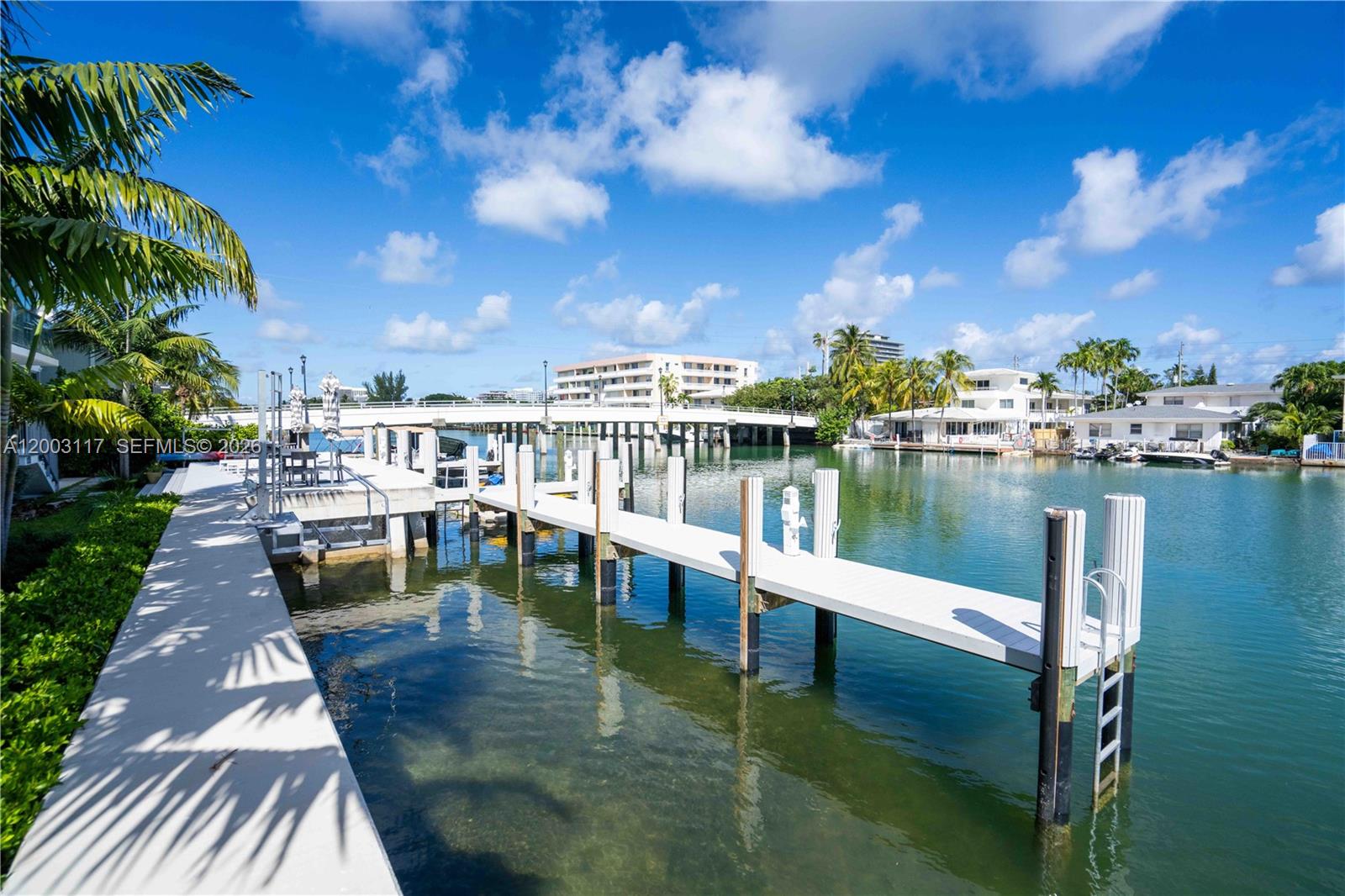 A white boat dock extends over clear water toward a bridge under a blue sky — 8425 Crespi Blvd, Miami Beach FL 33141, MIAMI BEACH, FL