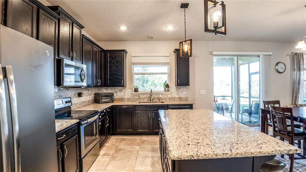 A kitchen features dark wood cabinets, granite countertops, a stainless steel refrigerator, and a center island — 2515 FONTAINE DRIVE, KISSIMMEE, FL
