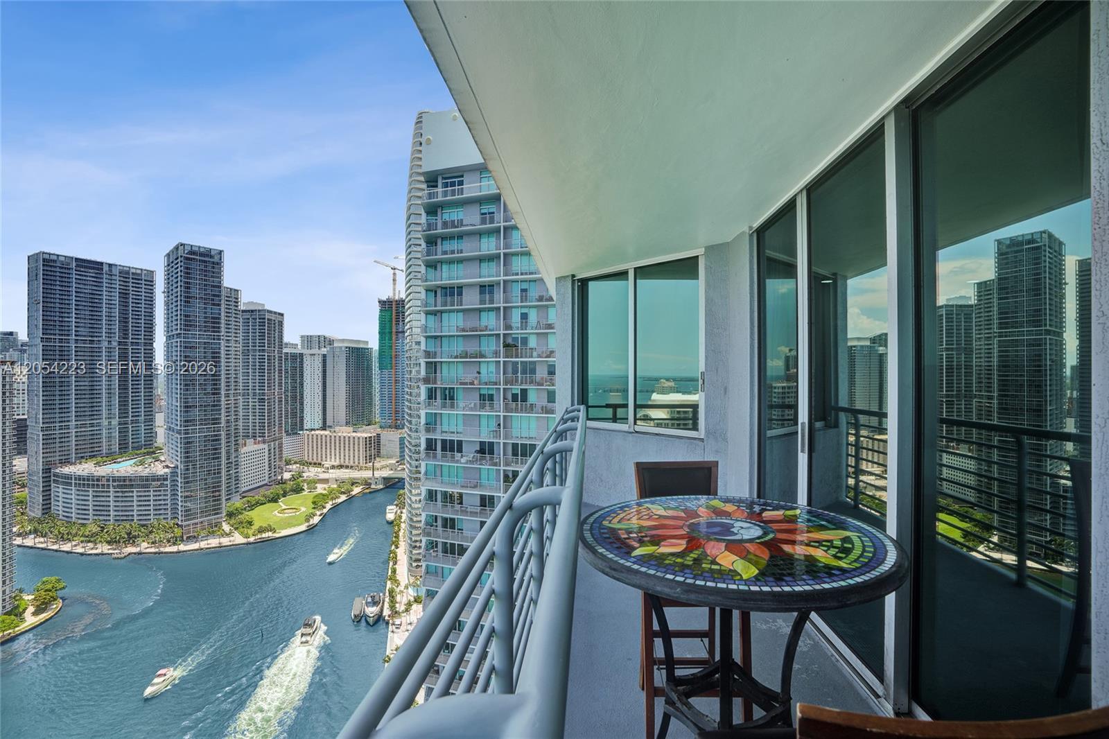 A balcony with a mosaic table overlooks a river surrounded by high-rise buildings — 335 S Biscayne Blvd # 3807, Miami FL 33131, MIAMI, FL